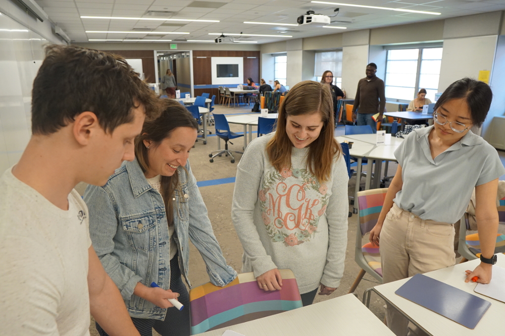 students gather around the ASC space to work on a problem together, looking down at a notebook